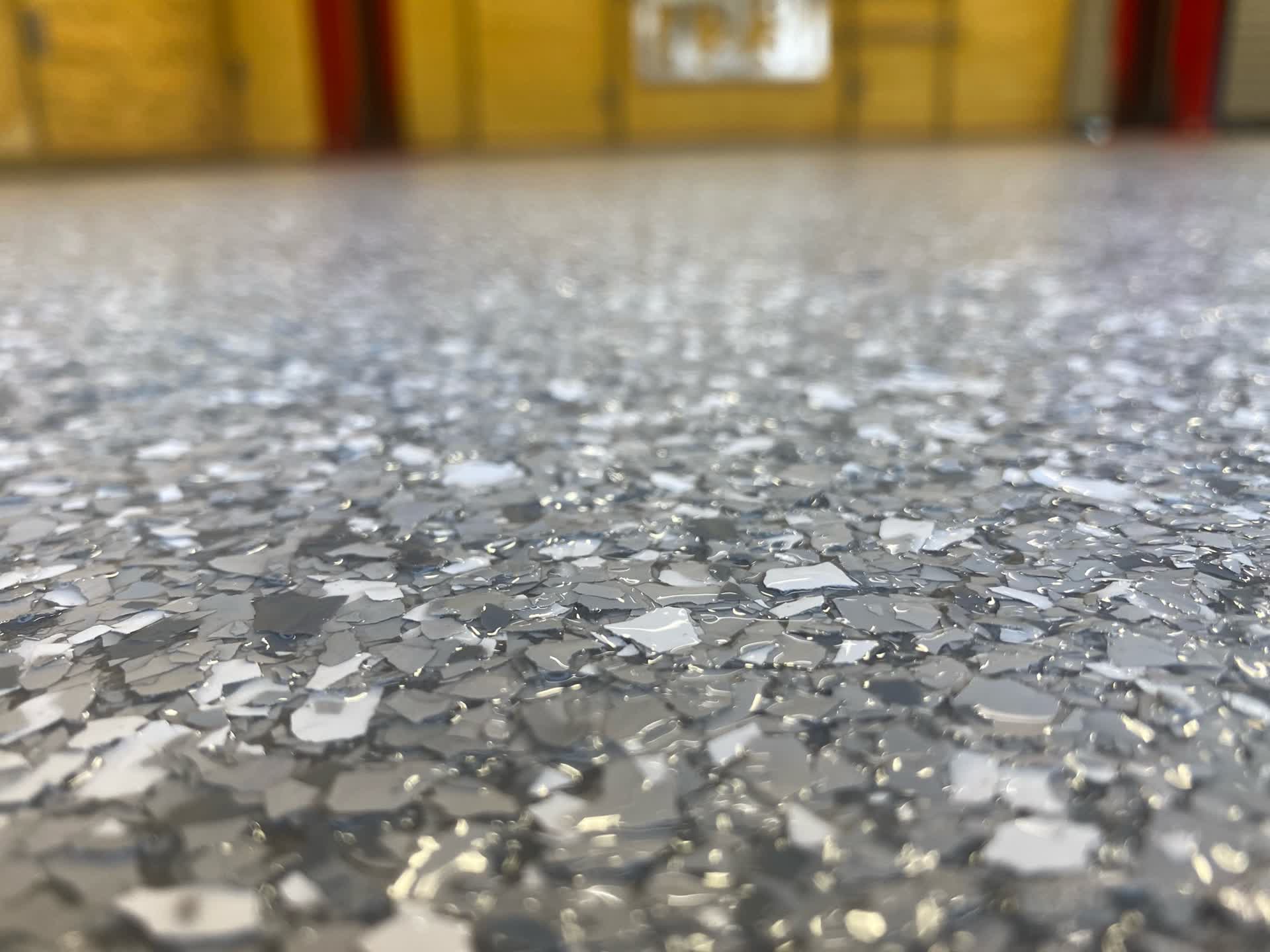 Grey and white flake floor in close view with yellow and red lockers blurred behind