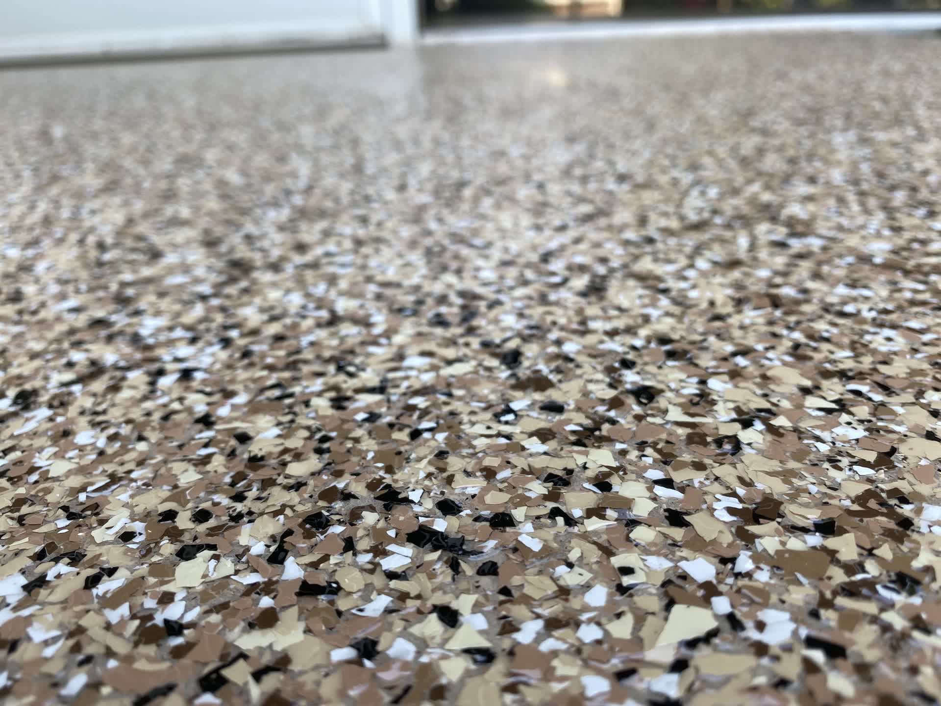 Tan, cream and black flake chips in a glossy coating with a doorway behind