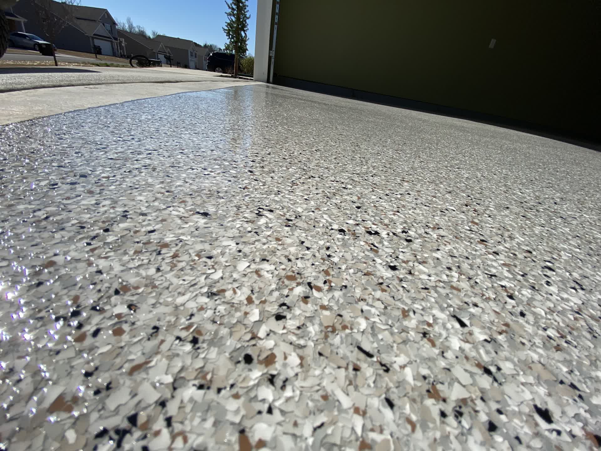 White and tan flake garage floor meeting the driveway, neighbouring houses in the background