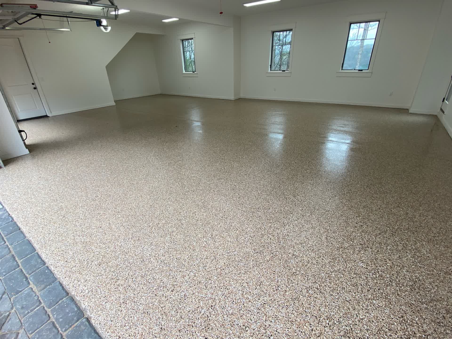 Cream and tan flake floor across a large empty garage with three windows and a paver apron in Laurel, Mississippi