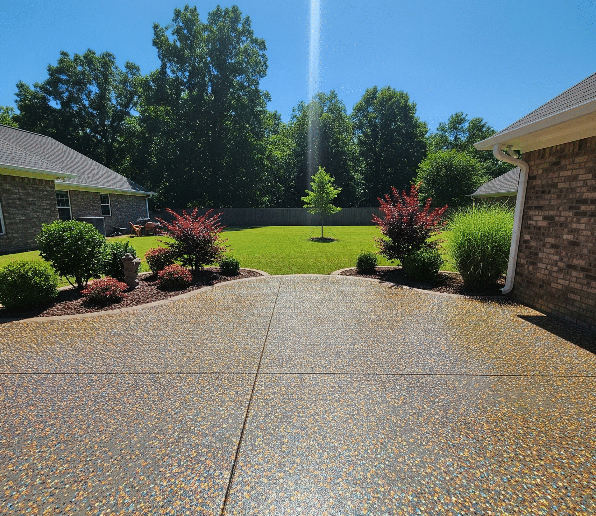 Tan and gray flake coating on a wide residential patio with landscaping and a lawn beyond in Mississippi