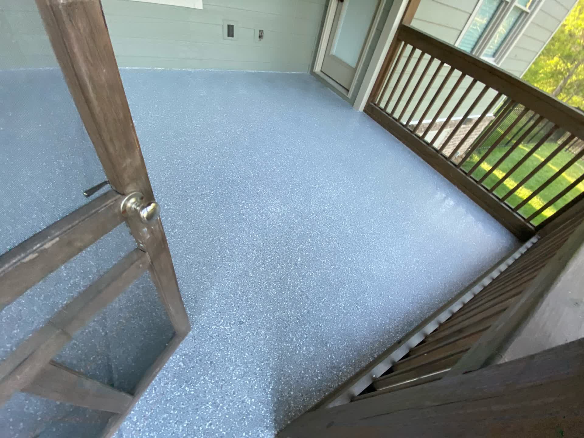 Blue-grey flake coating on a covered porch floor with a wooden rail and lawn beyond